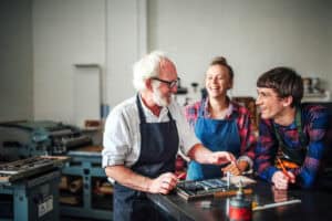 Oberhandwerker lacht mit junger Handwerkerin und Handwerkerin in Buchdruckwerkstatt Von imagesourcecurated