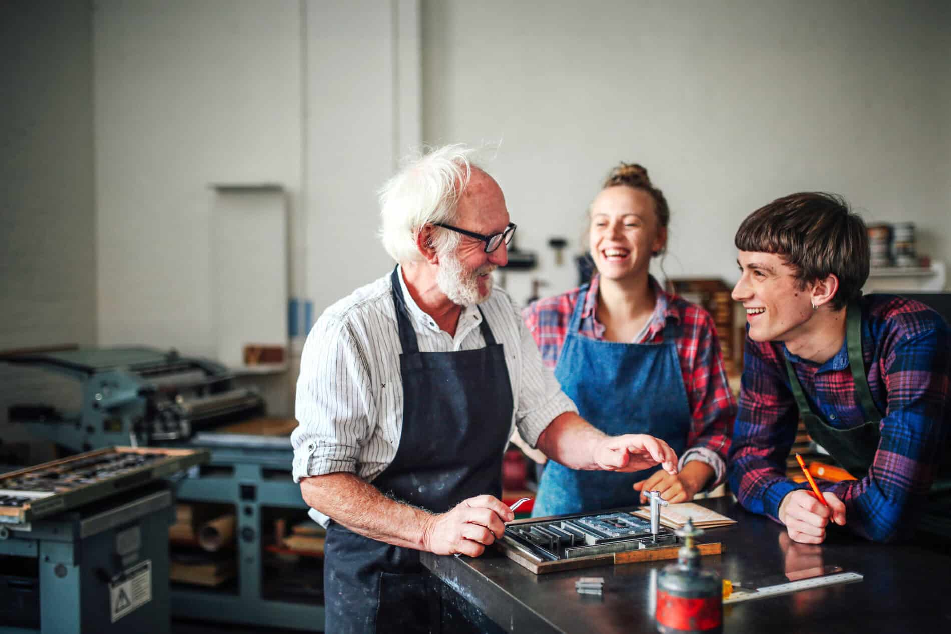 Oberhandwerker lacht mit junger Handwerkerin und Handwerkerin in Buchdruckwerkstatt Von imagesourcecurated